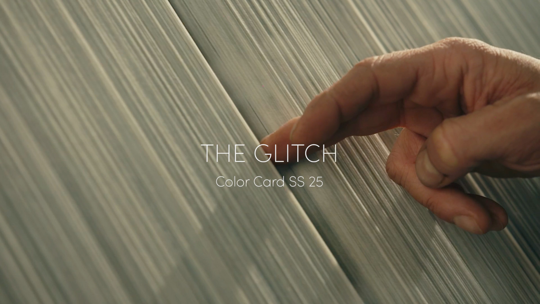 Dita di una mano che scorrono sui fili di un telaio, in mezzo alla fato la scritta "the glitch color card SS25"