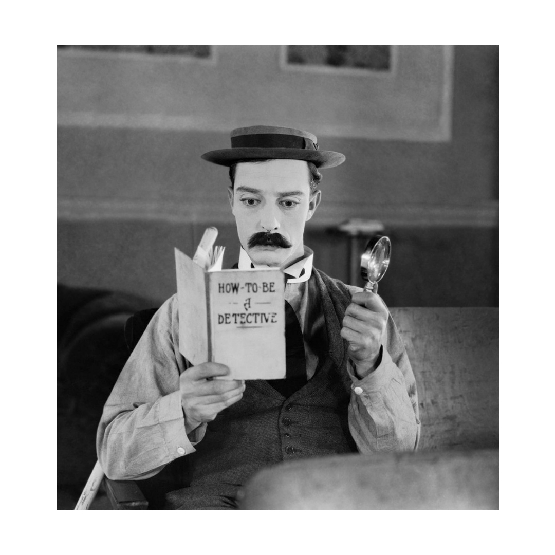 Foto in bianco e nere do un attore che legge un libro con una lente di ingrandimento in mano