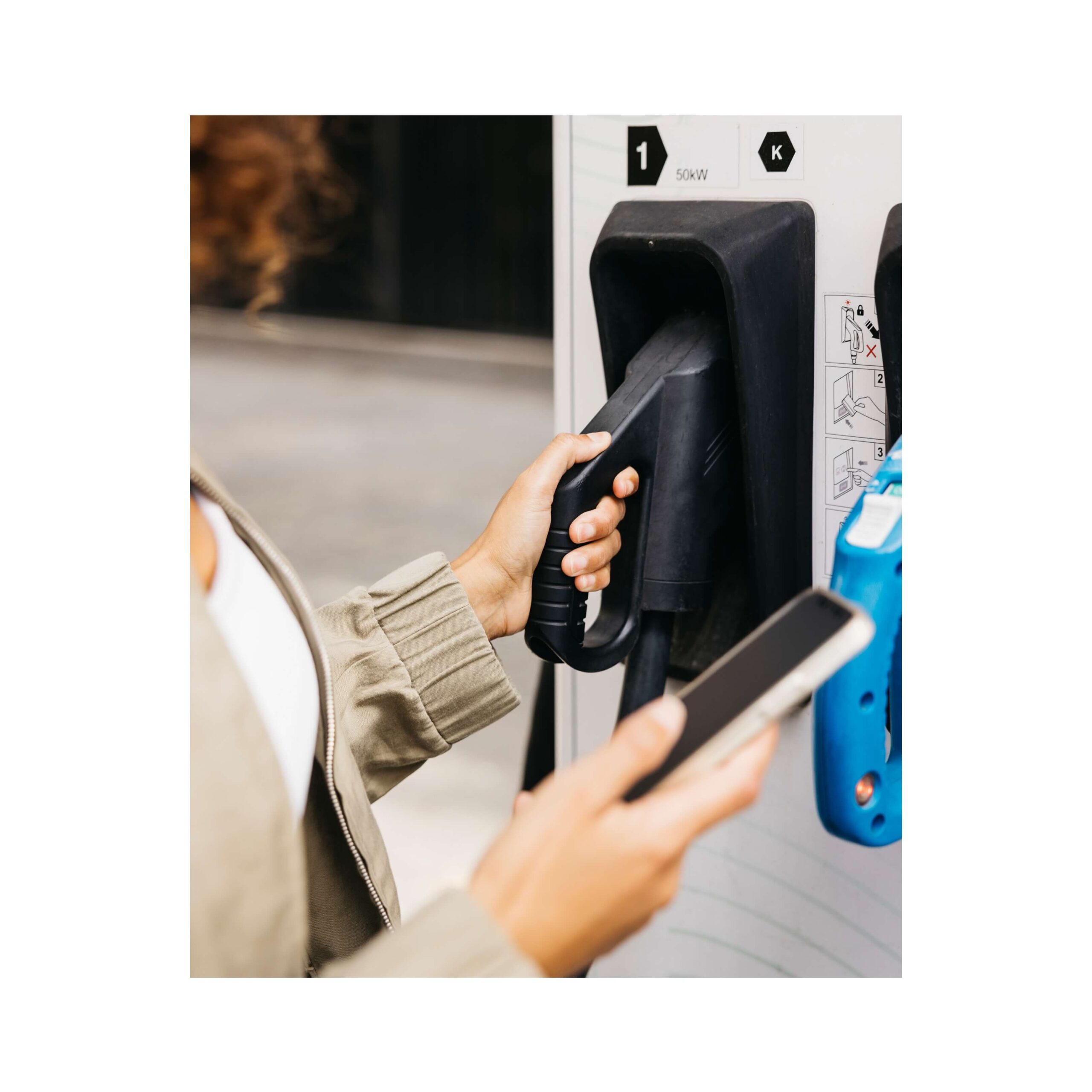 mano di donna intenta a prendere pompa di ricarica elettrica con in mano cellulare utilizzato per individuare la colonnina di ricarica