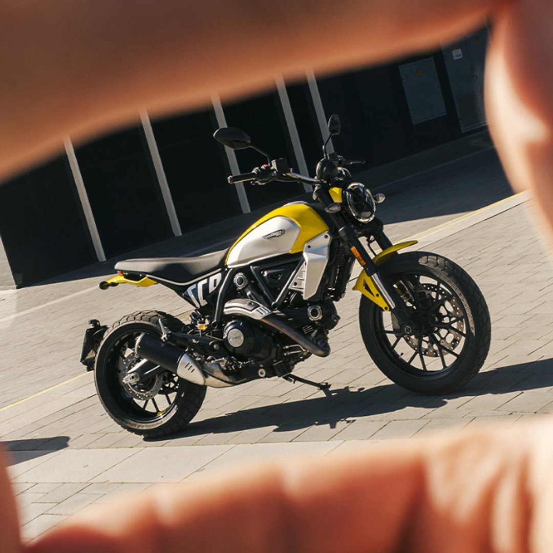 foto di una ducati scrambler inquadrata da delle dita